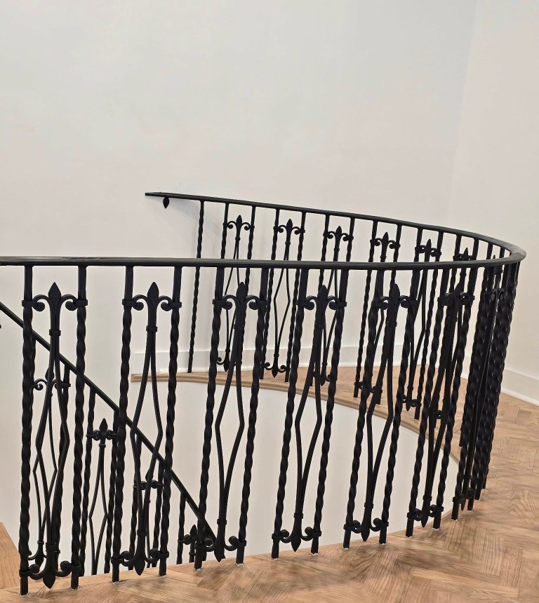 Curved black iron staircase railing with diamond and fleur-de-lis panels