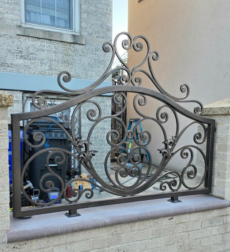 Ornamental iron fence panel with scrollwork on a brick wall