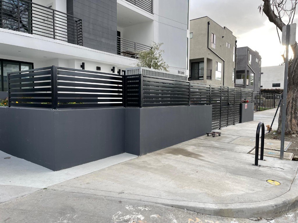 Black horizontal-slat steel fence and gate along a sidewalk